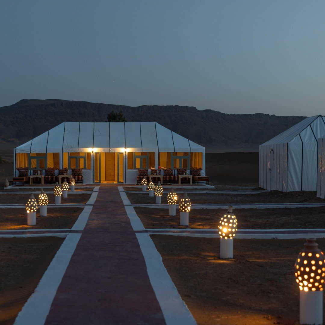 Elegant desert camp lit by ornate Moroccan lanterns along a
pathway at dusk with mountain backdrop --- Morocco Live Trips 2-day
Zagora desert getaway