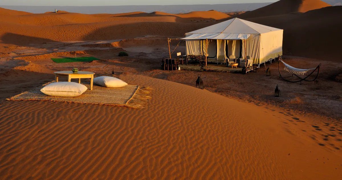 Luxury Berber glamping tent on rippled red Sahara sand dunes at
sunrise with Moroccan cushions and lanterns -- Morocco Live Trips
authentic desert camp experience